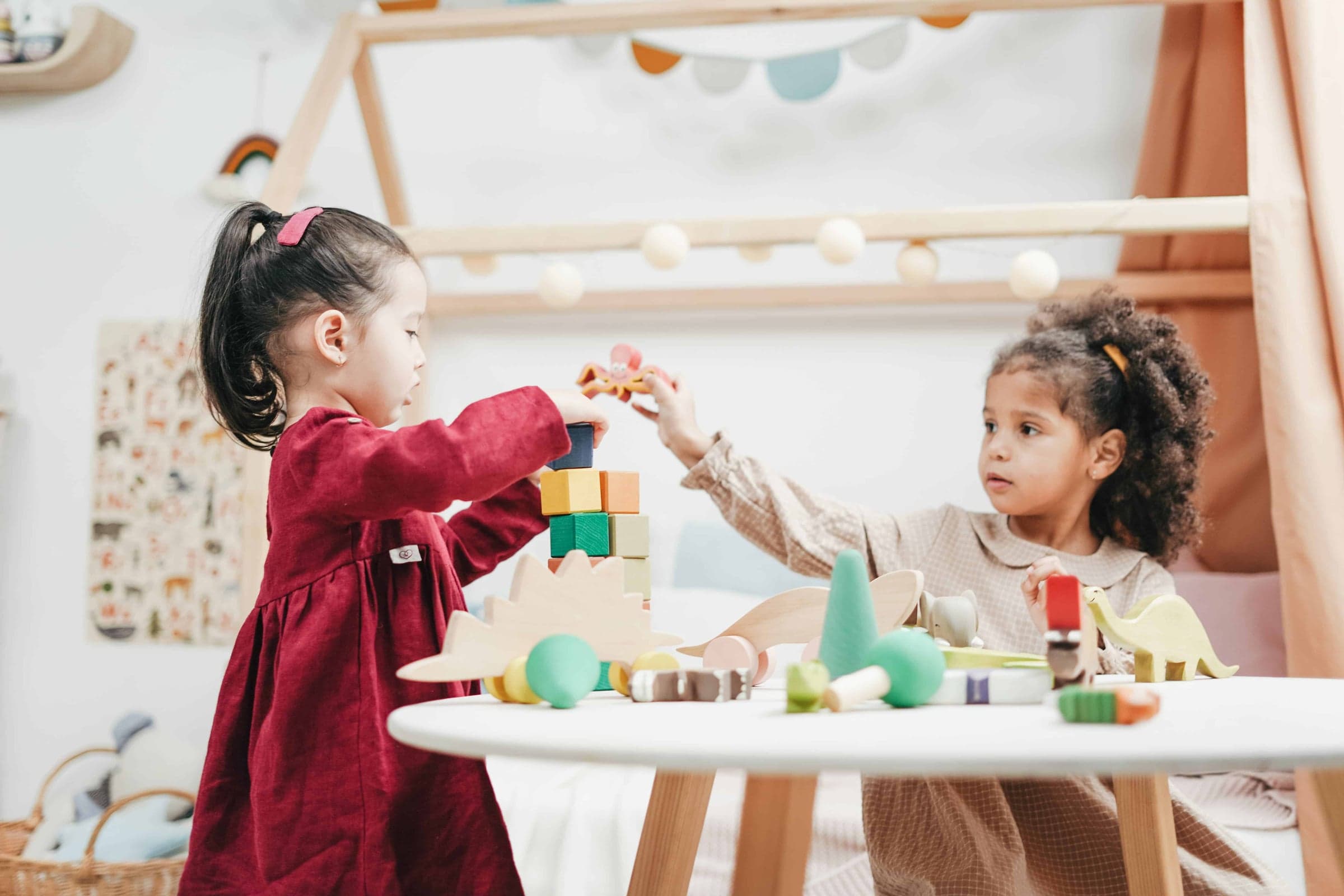 Zwei Mädchen spielen gemeinsam mit bunten Holzbausteinen an einem Kindertisch